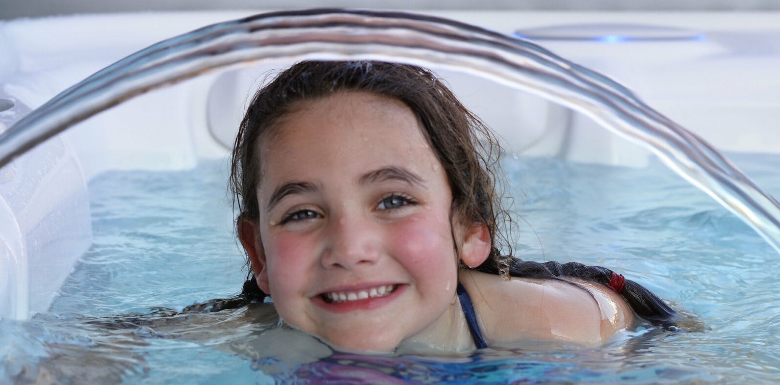 Smiling young girl in a hot tub with a water fountain going over her head.